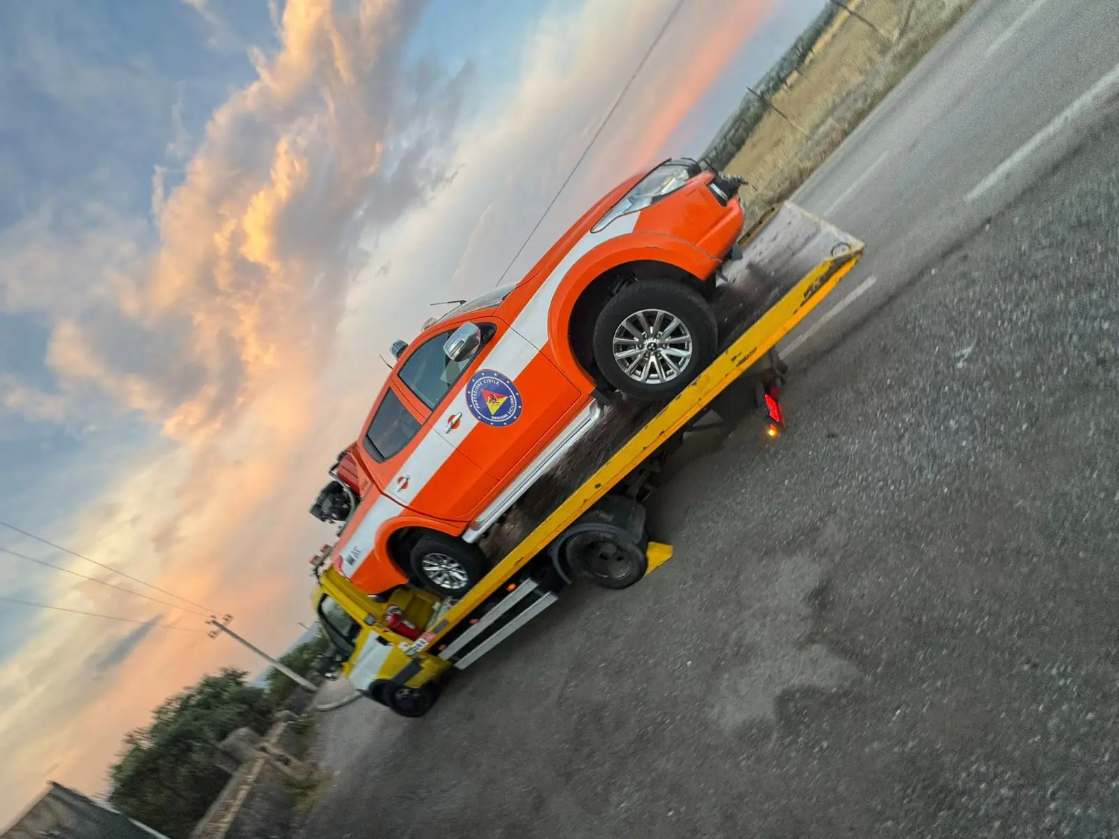 Pick-up arancione caricato sul pianale del carroattrezzi al tramonto